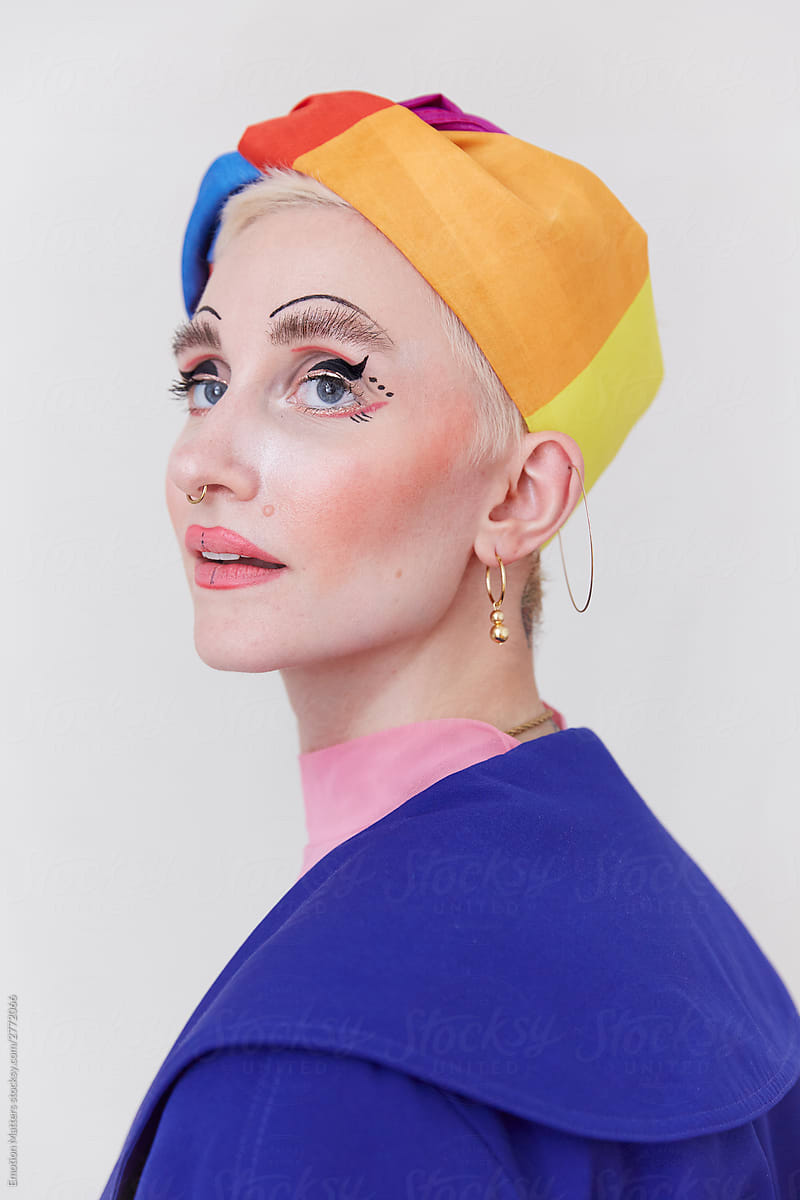 A stylish woman wearing a beautiful rainbow hat and a unique makeup look.