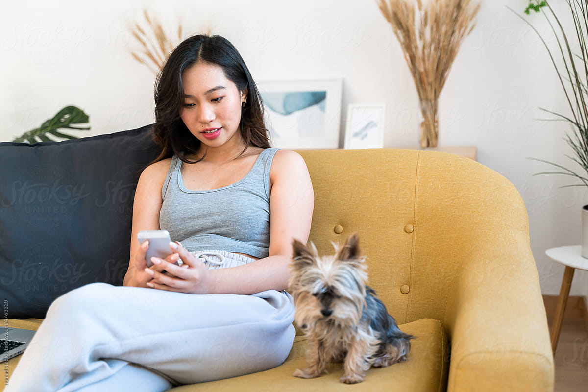 Woman using a mobile phone sitting on a sofa with her dog.