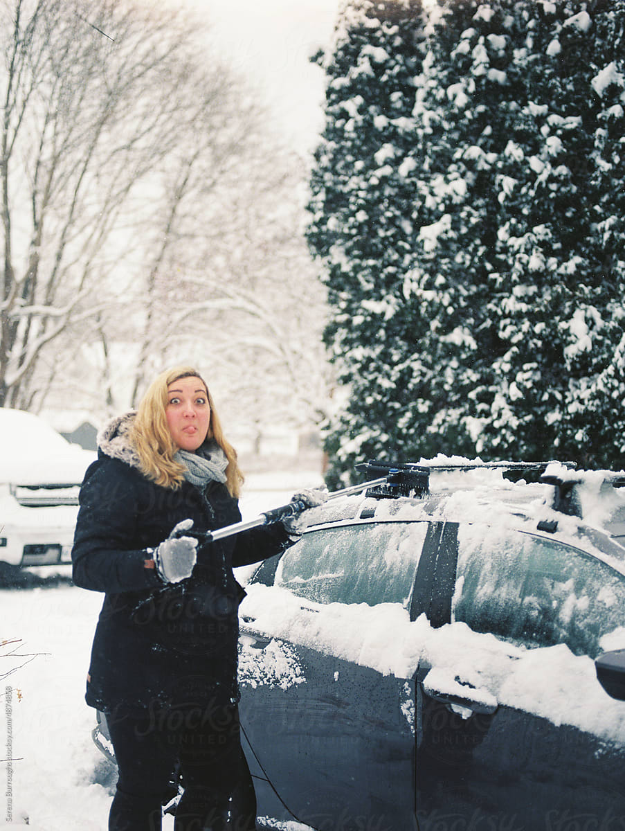 Woman clearing snow off her car in winter