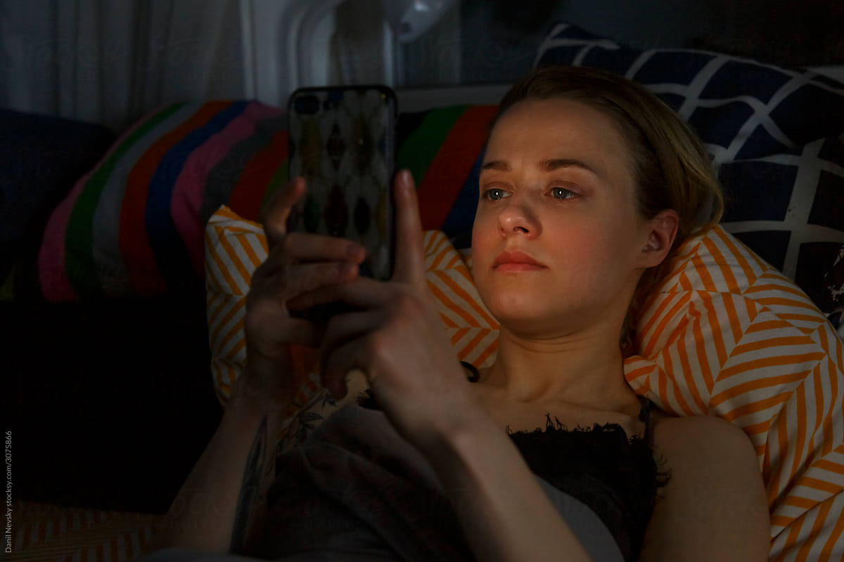 Woman lying on pillows and using smartphone at night