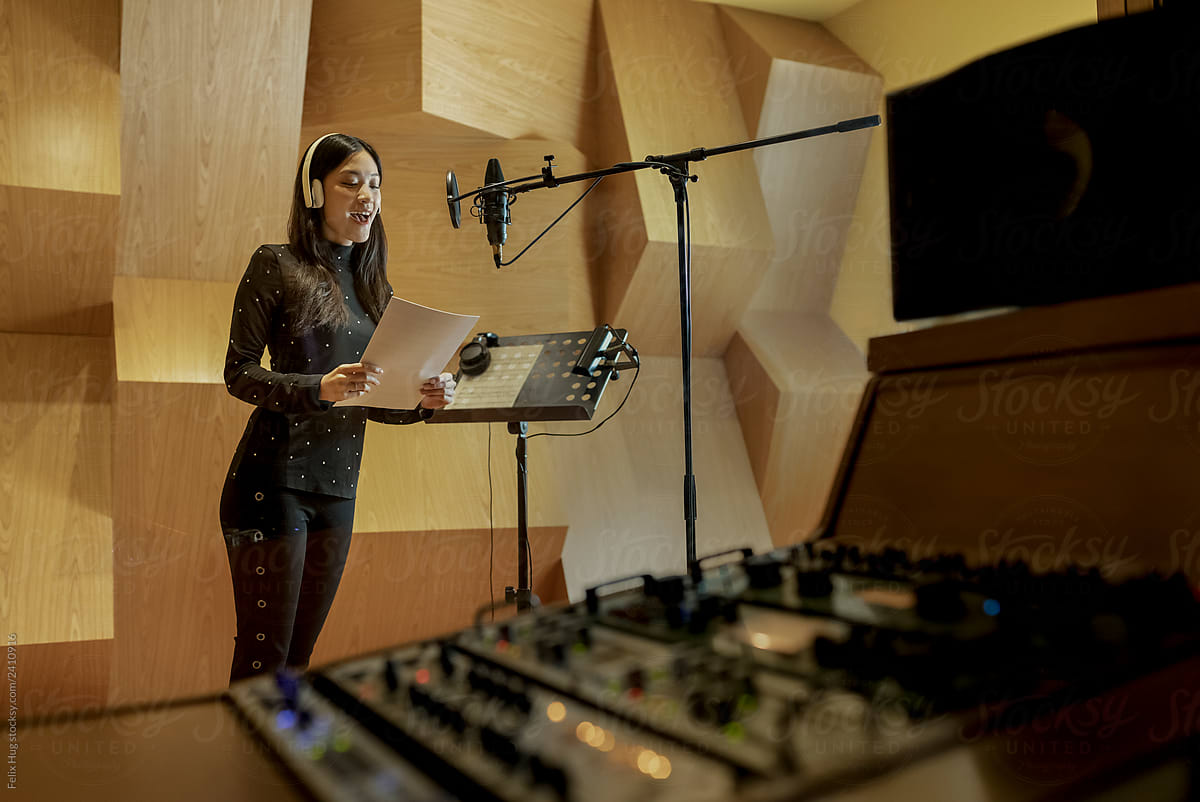 A woman is singing a song from a musical paper while in a recording studio in Singapore.