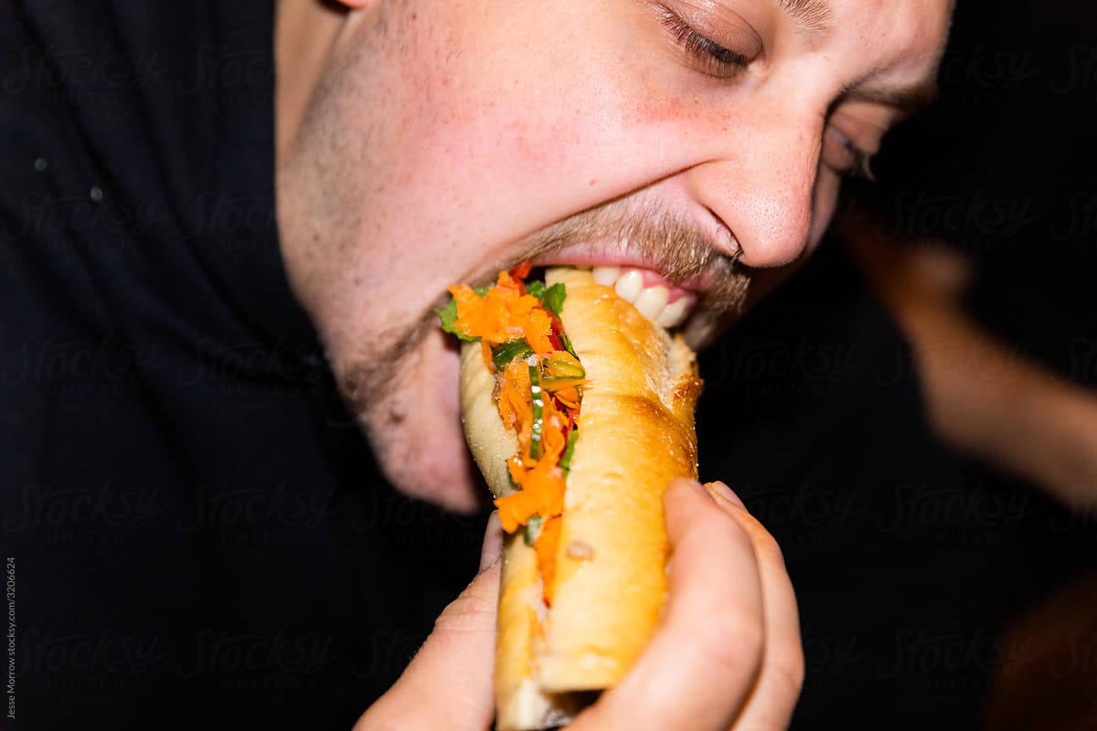 young male eating banh mi sandwich