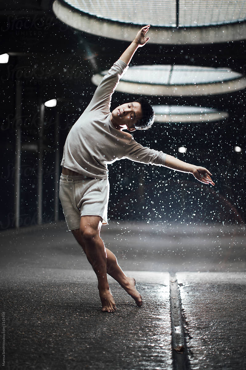 An Asian man dancing in the rain in an unusual urban setting