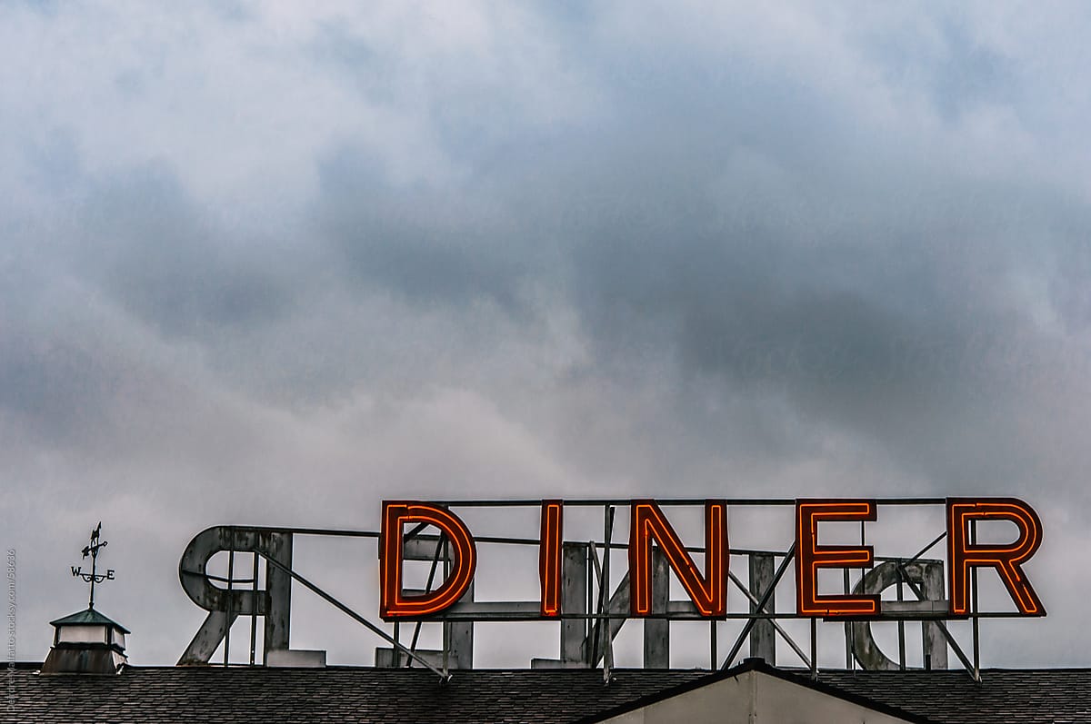 Red neon diner sign on a roof with clouds