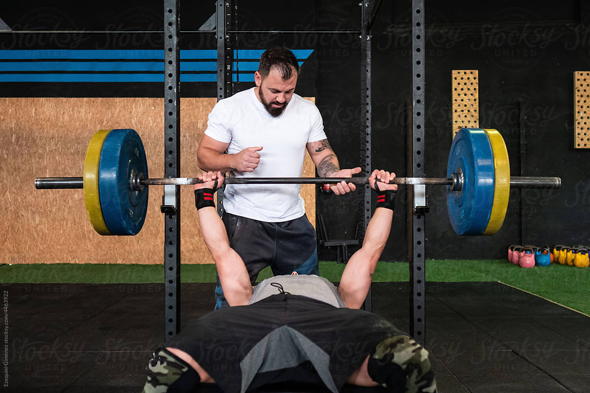 Bearded trainer helping athlete to lift barbell