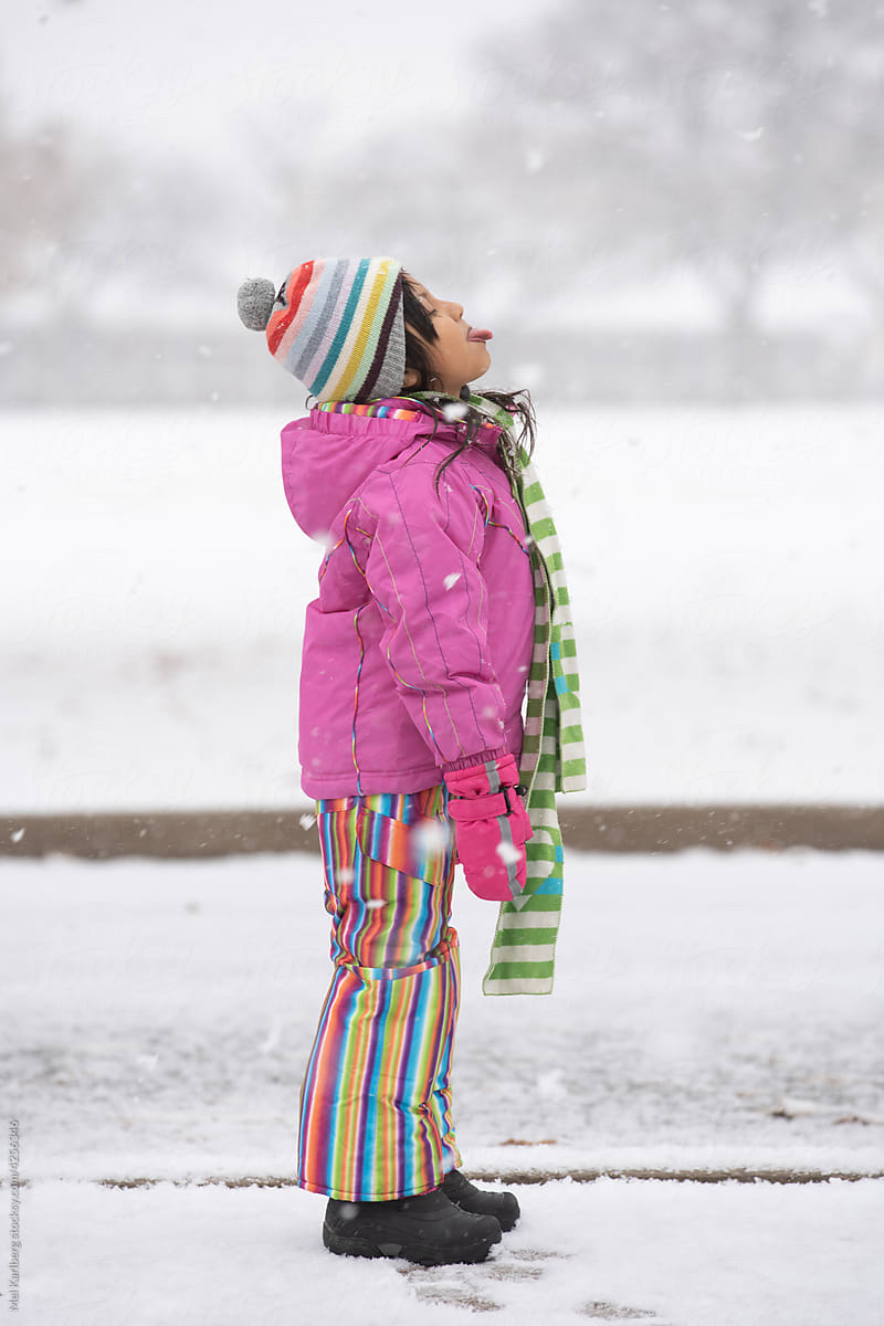 Girl in pink rainbow snowsuit catching snowflakes 2