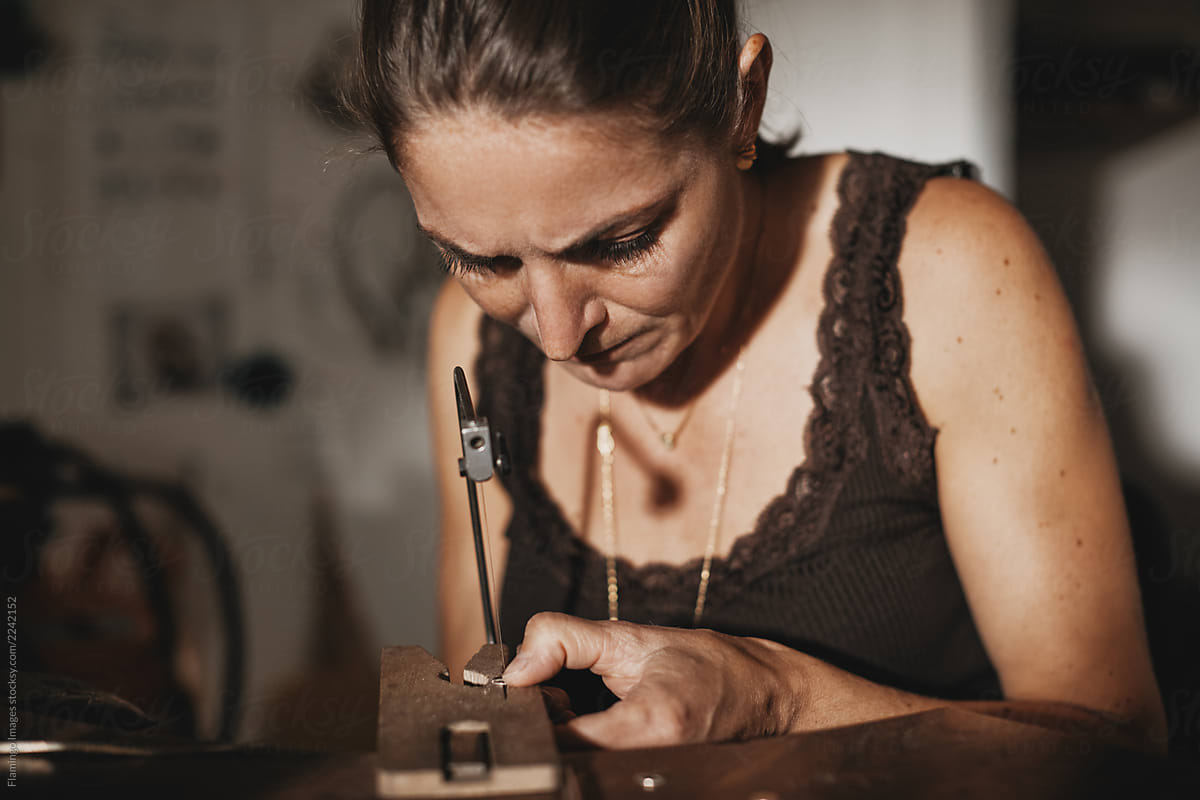 Female jeweler sitting at her studio workbench using a saw