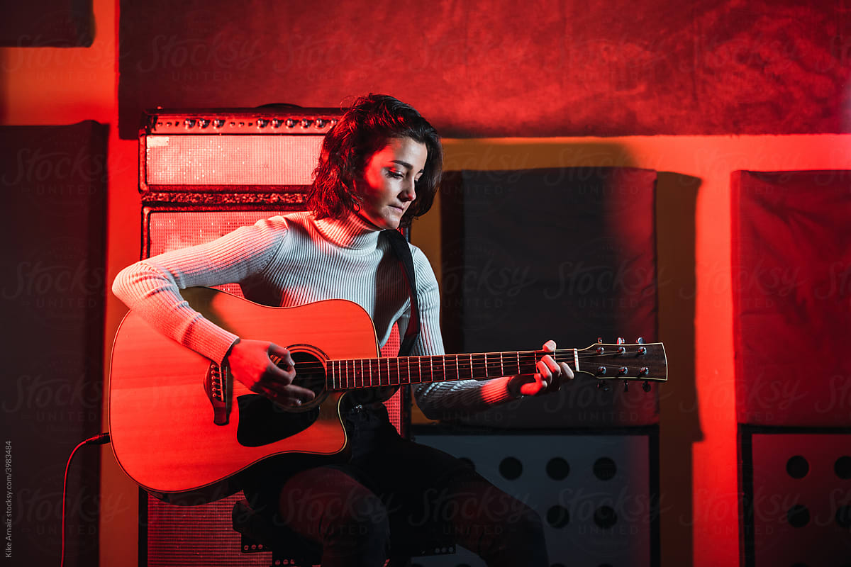 Smiling lady playing on guitar in red neon lights in music studio