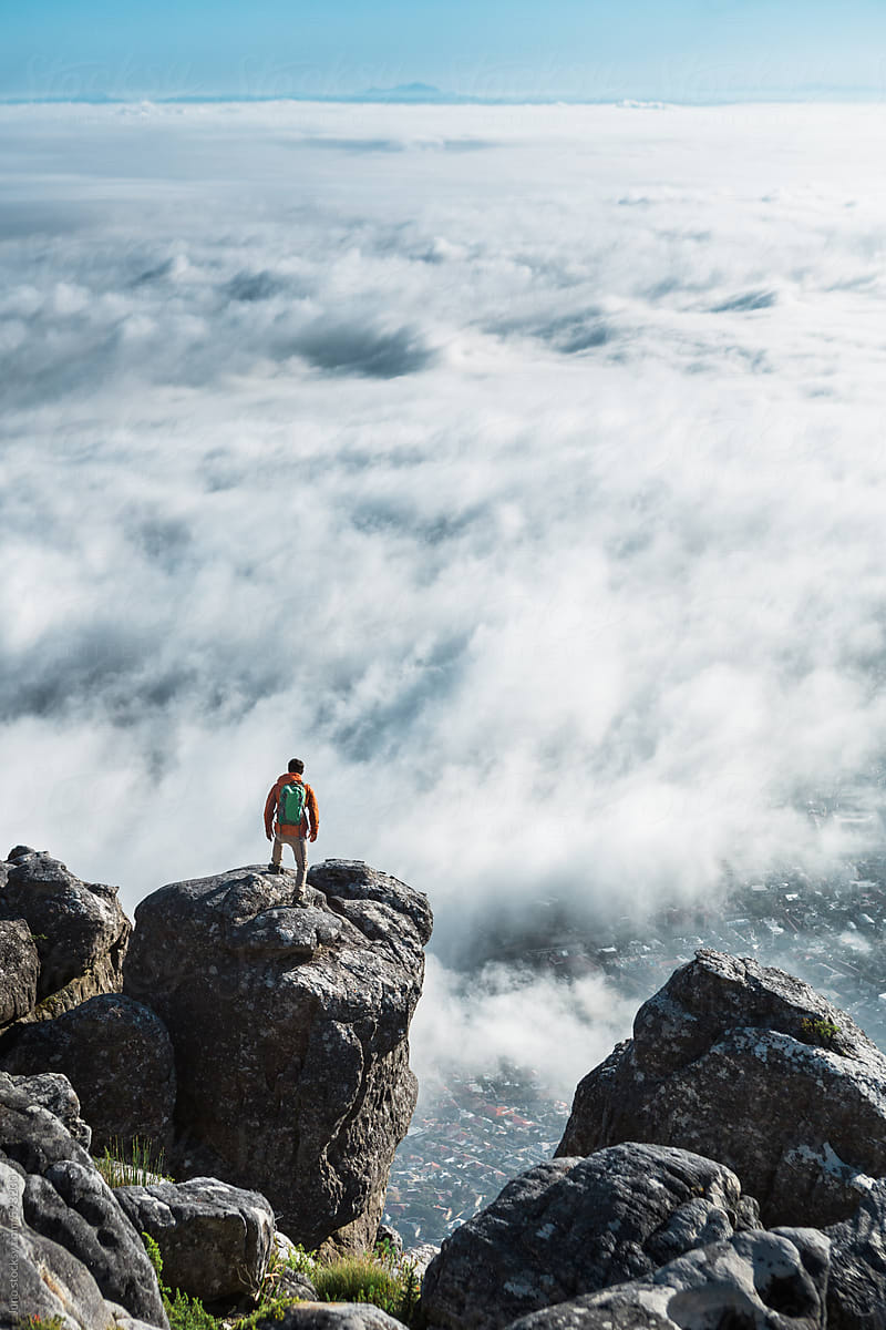 Male hiker with backpack on a mountain summit overlooking clouds