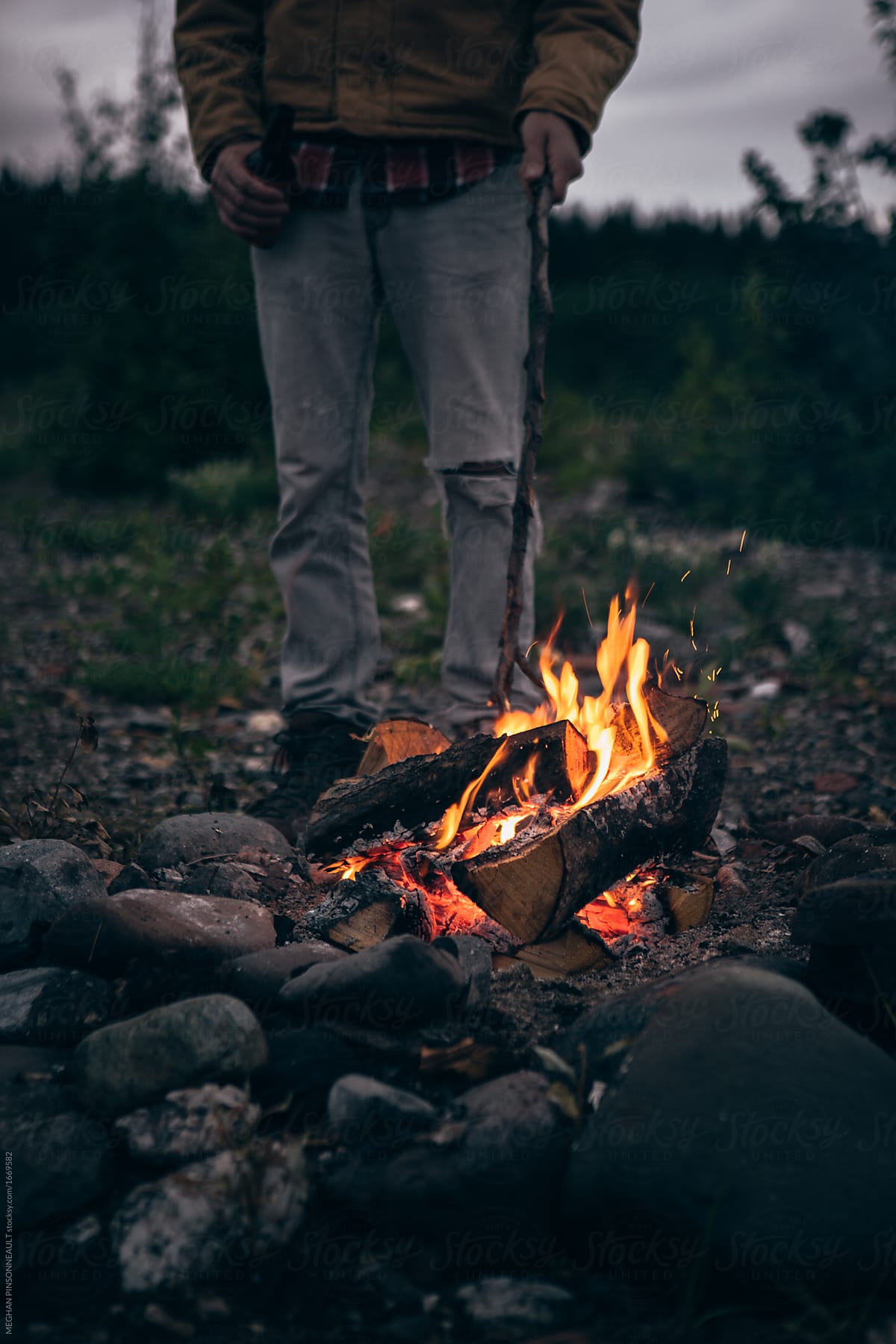 Man Poking Campfire at Dusk