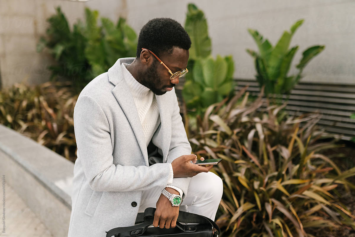 Black elegant man browsing smartphone on street