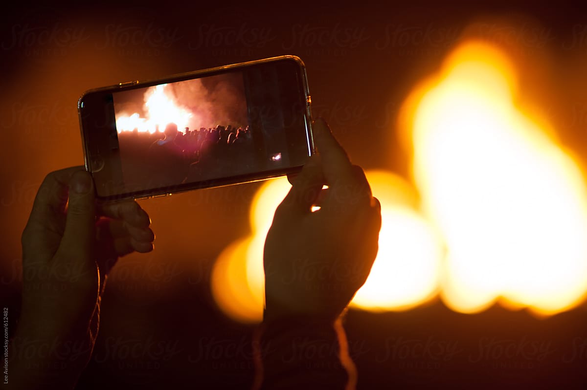 people gathered around a large fire being filmed on a mobile device