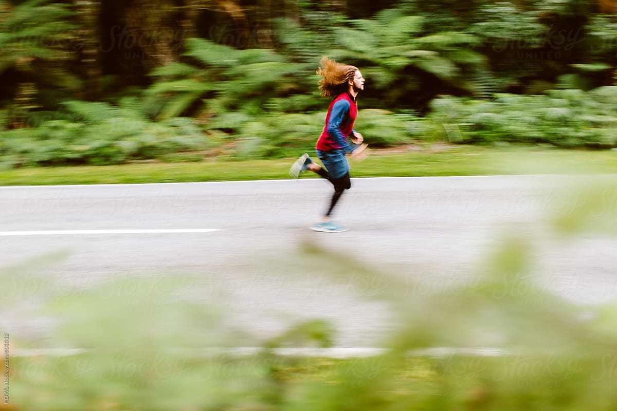 A long haired man running down an empty New Zealand road