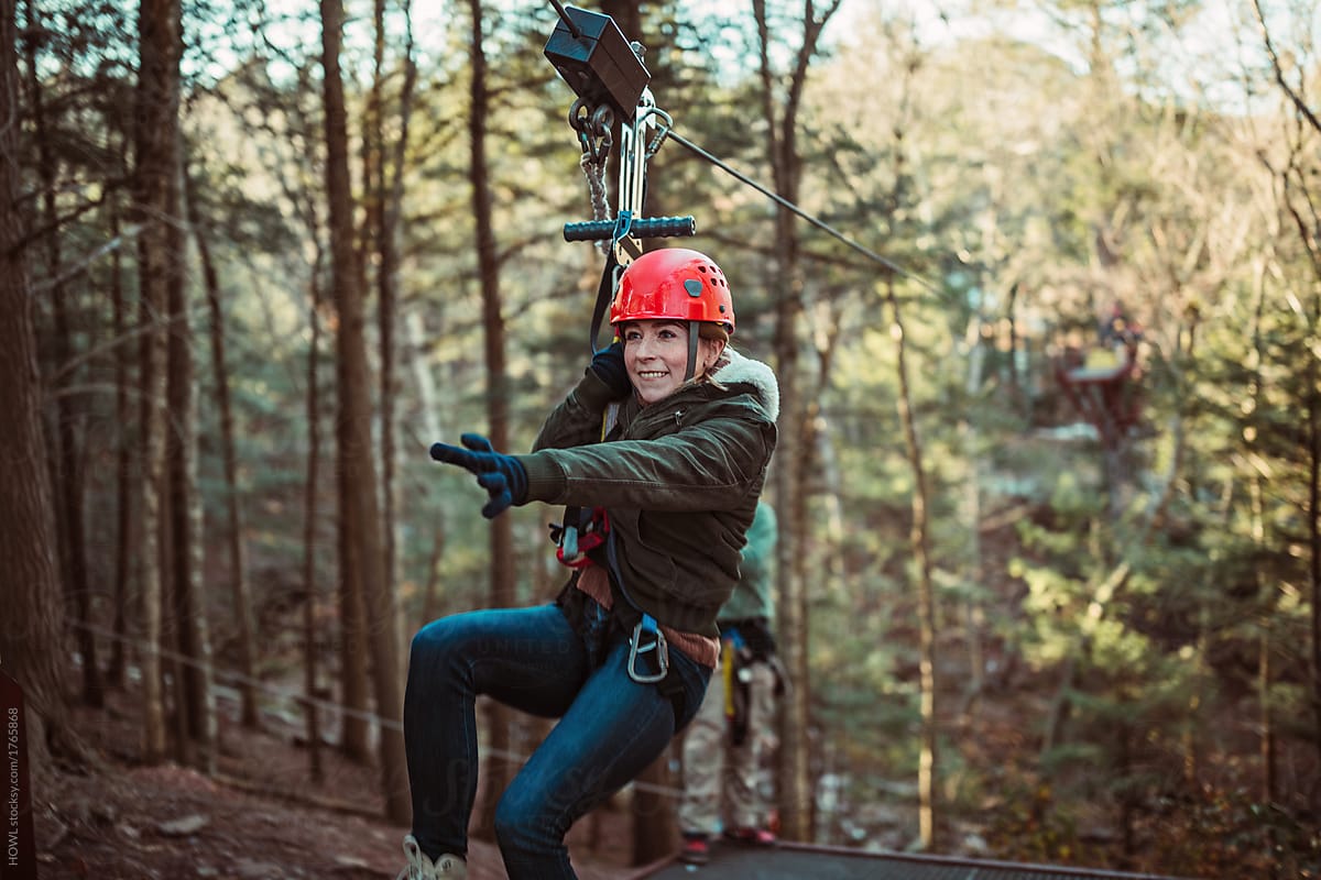 Young woman smiles while zip lining through the woods in upstate New York