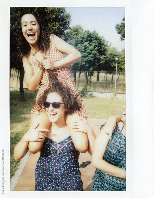 Polaroid shot of brunette pulling her friend\'s hair while sitting on her shoulders