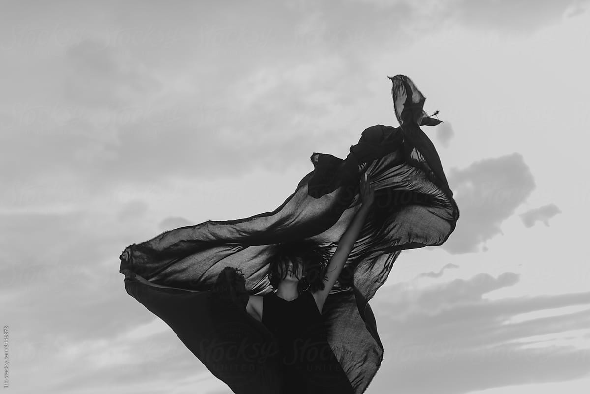 Woman inside of a dark mysterious black cloth blowing in the wind in the desolate desert