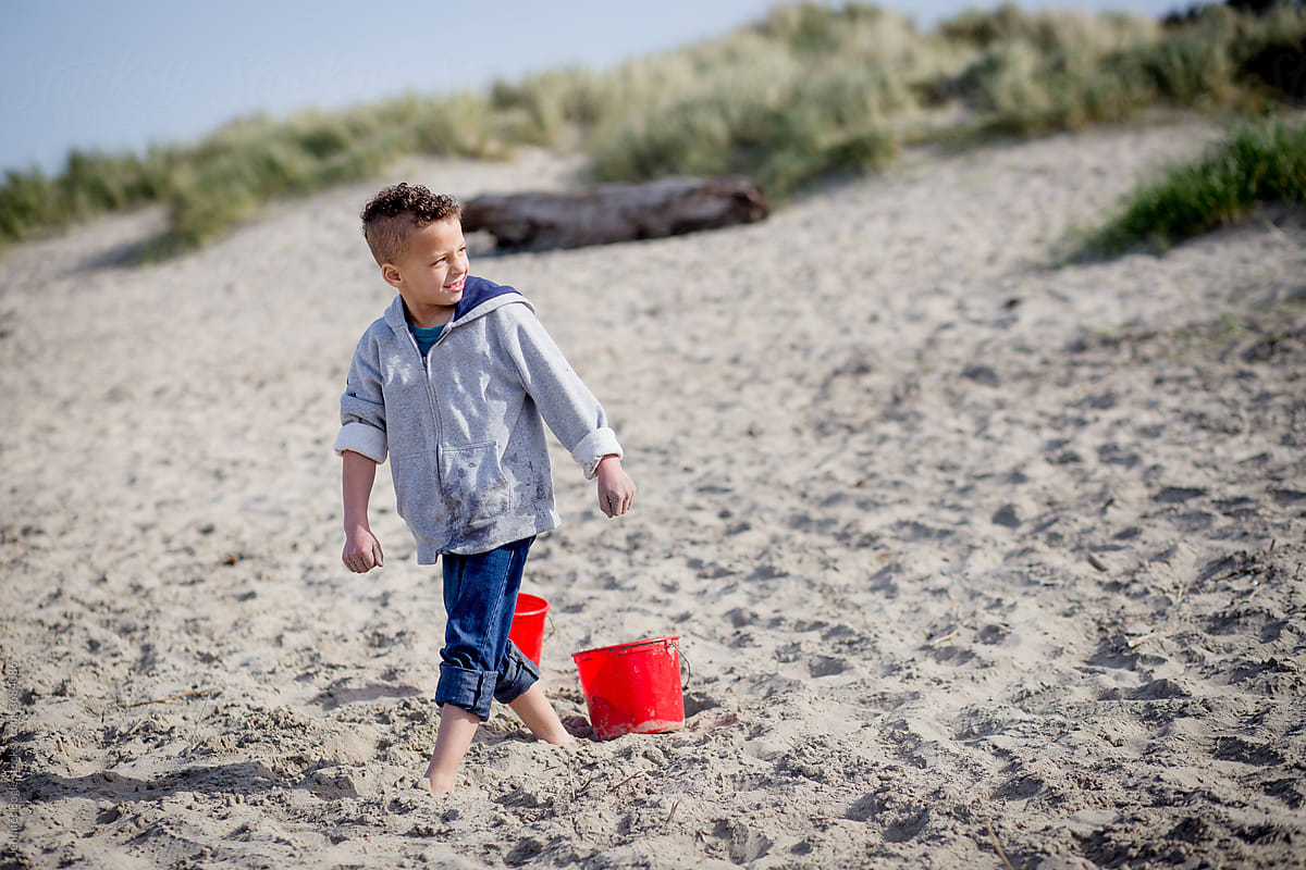 Smiling boy plays on sandy beach with bucket