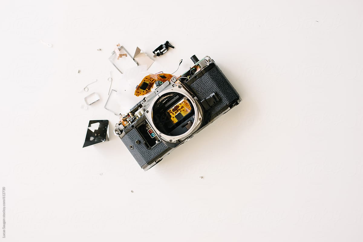 A broken parts camera laying on it\'s back with parts scattered on a table.