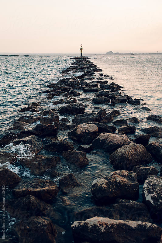 A lighthouse at sunset surrounded by water and rocky path, on focus