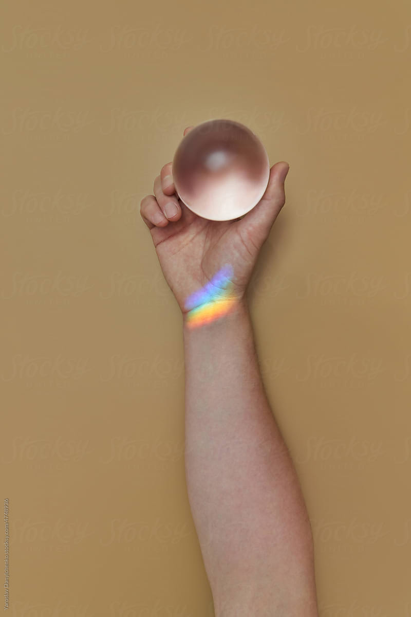 Person\'s hand holding crystal globe with rainbow.