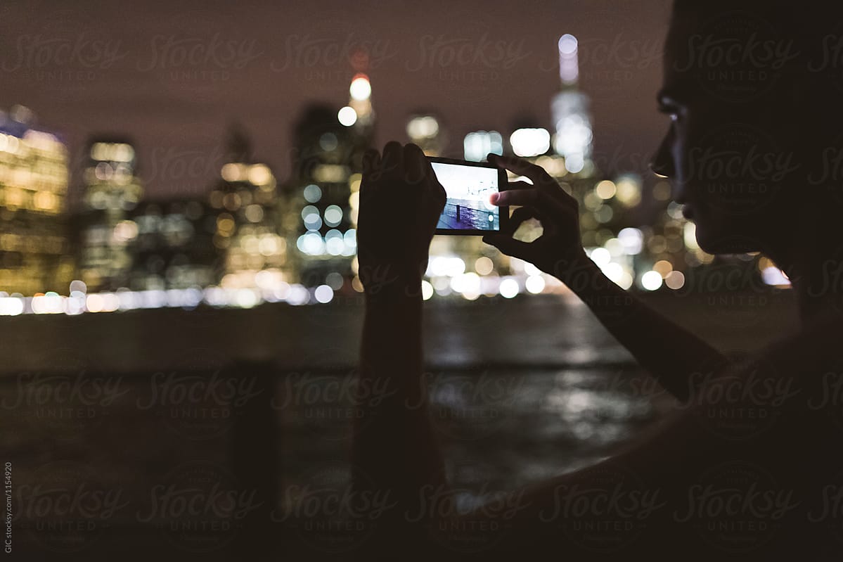 Young woman using technology at night against New York skyline