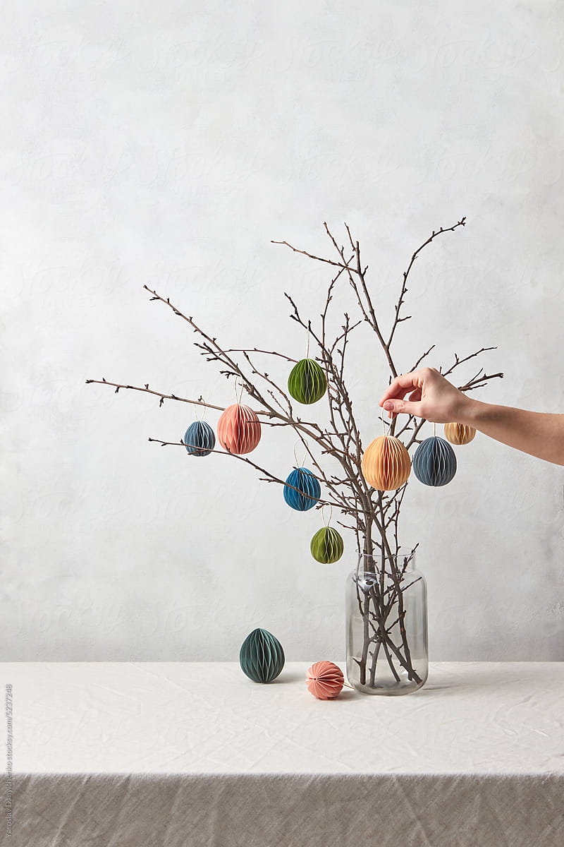 Paper Easter ornaments hung on branches by woman.