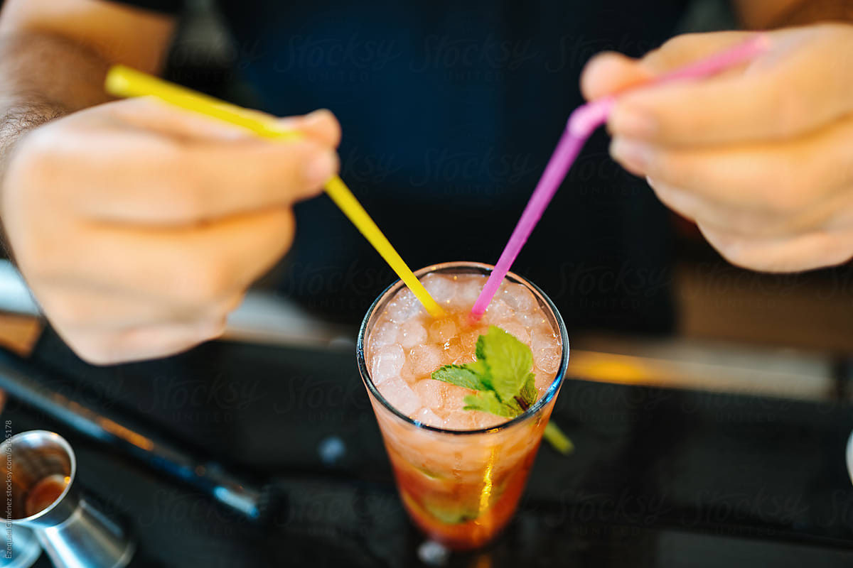 Crop barman putting straws into cocktail
