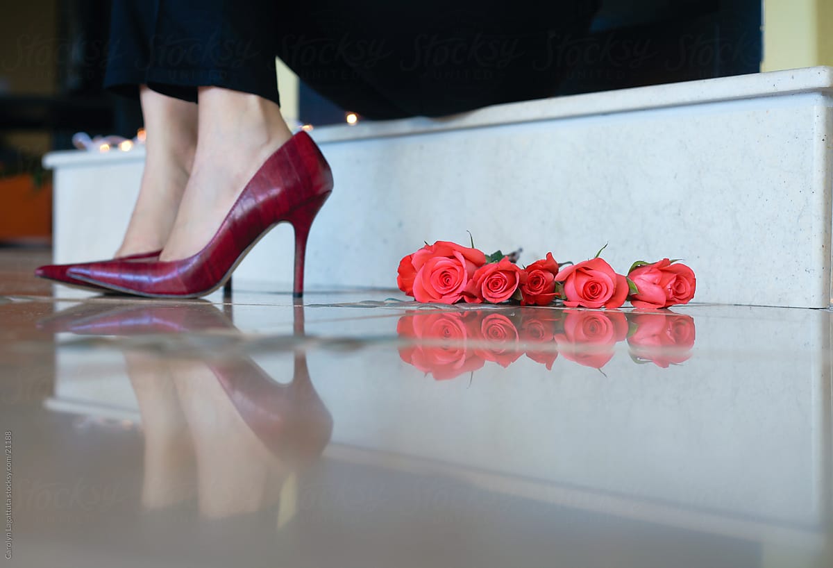 Woman in red heels with roses next to them sitting on the fireplace