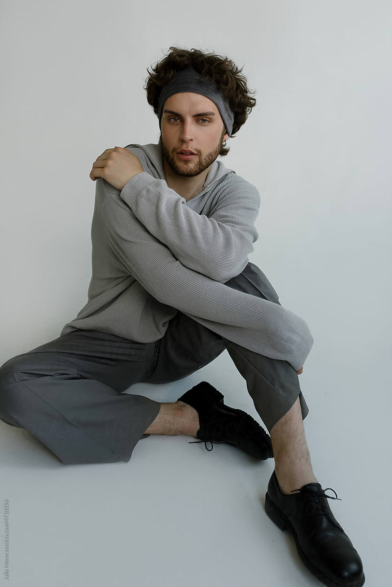 Stylish guy with curly hair sits in a grey sweater and a headband