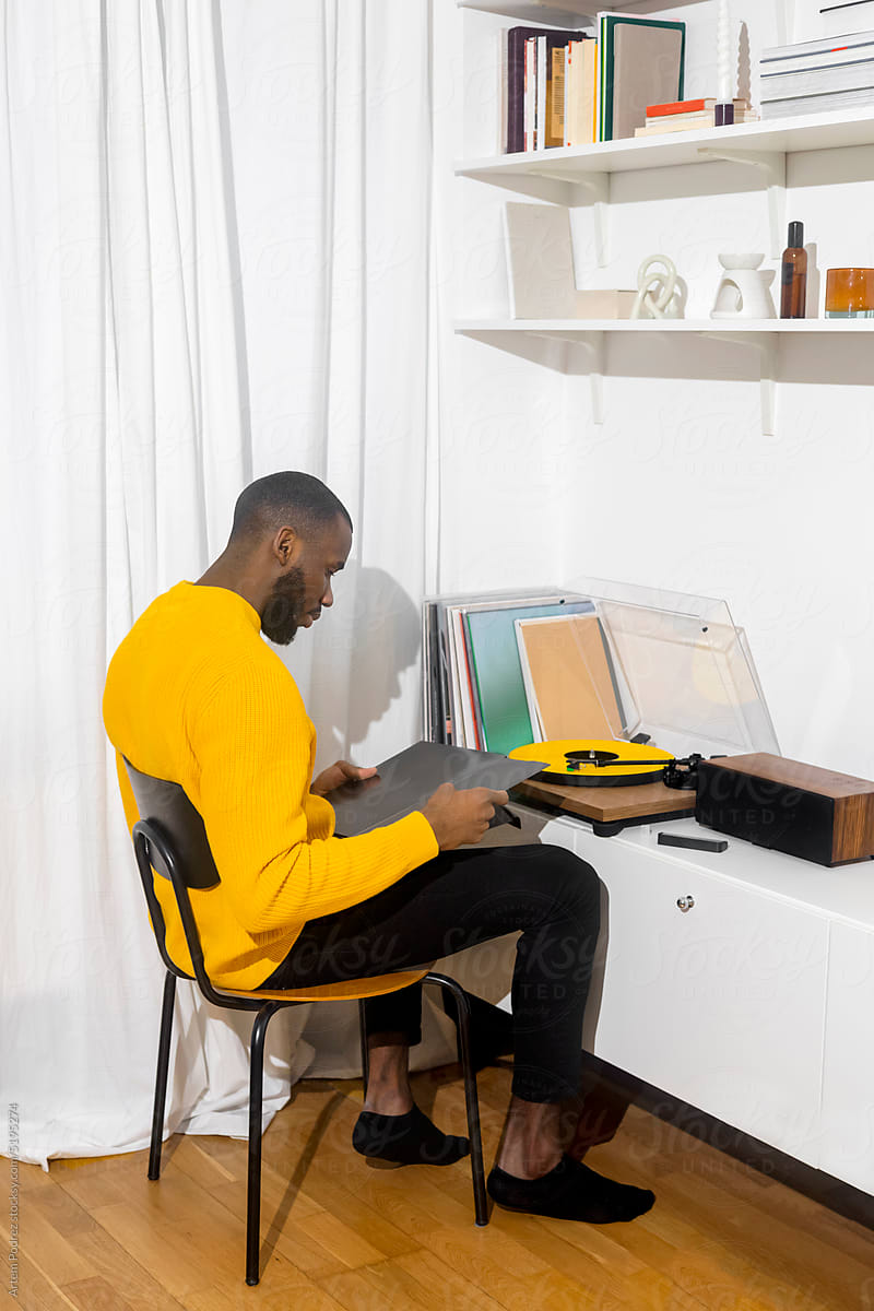 A black man in a yellow sweater listens to music