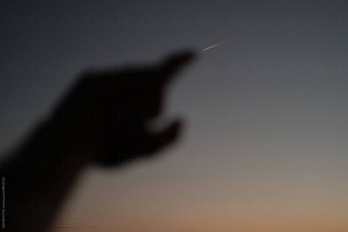 Hand pointing to plane flying in the sky.