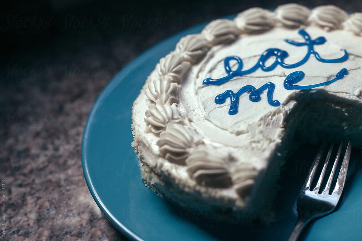 White cake that says Eat me on the top in blue letters