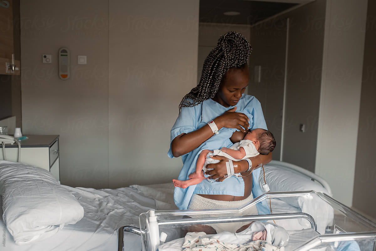 Black mom breastfeeding infant near hospital bed