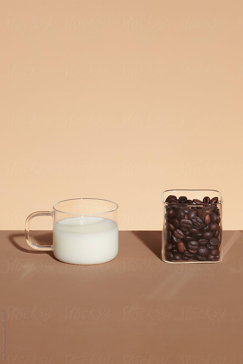Coffee beans and glass of milk on a brown background