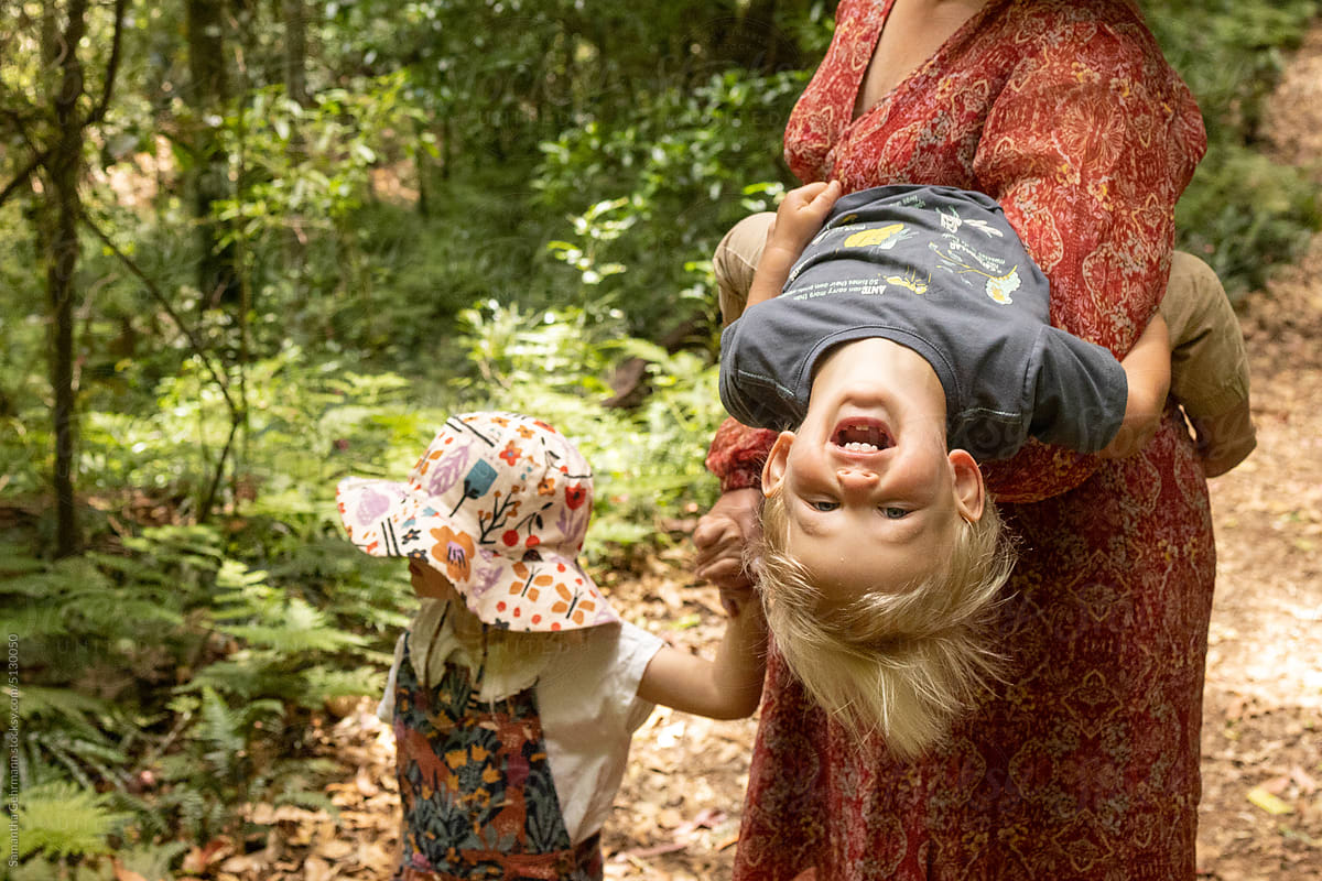 woman playfully tips son upside down on a walk