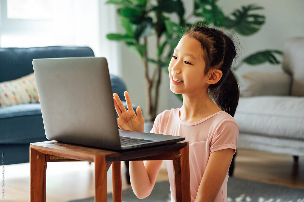 Little girl greeting online teacher using laptop