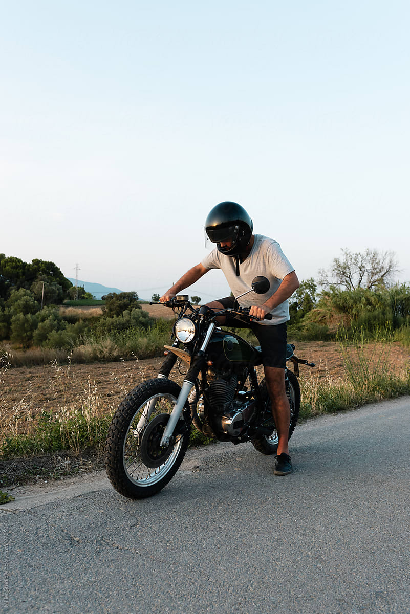 Biker in helmet starting motorcycle near meadow