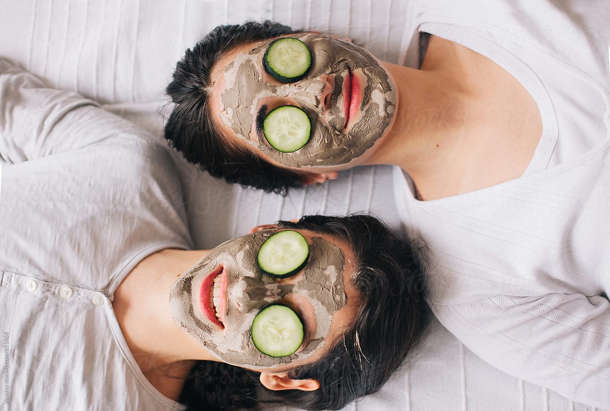 Two beautiful women with facial masks and cucumbers on their faces