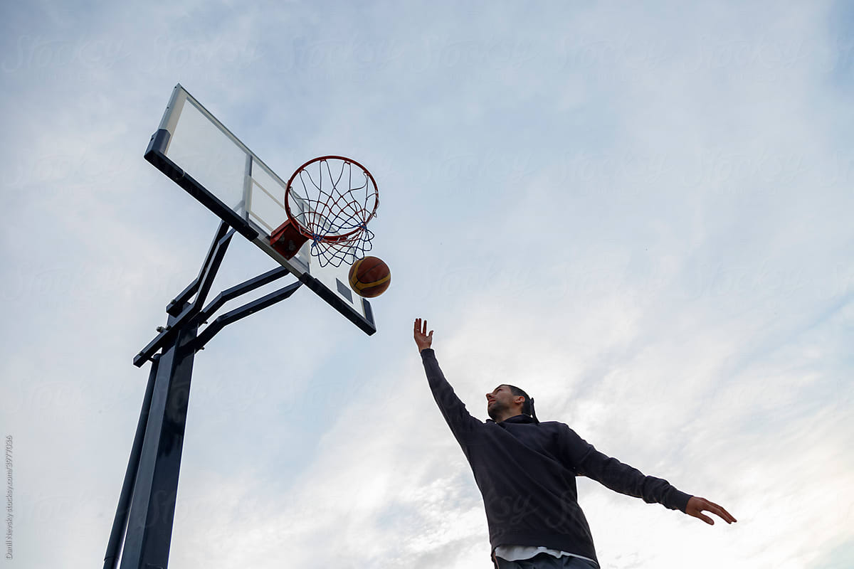 Man playing basketball against cloudy sky
