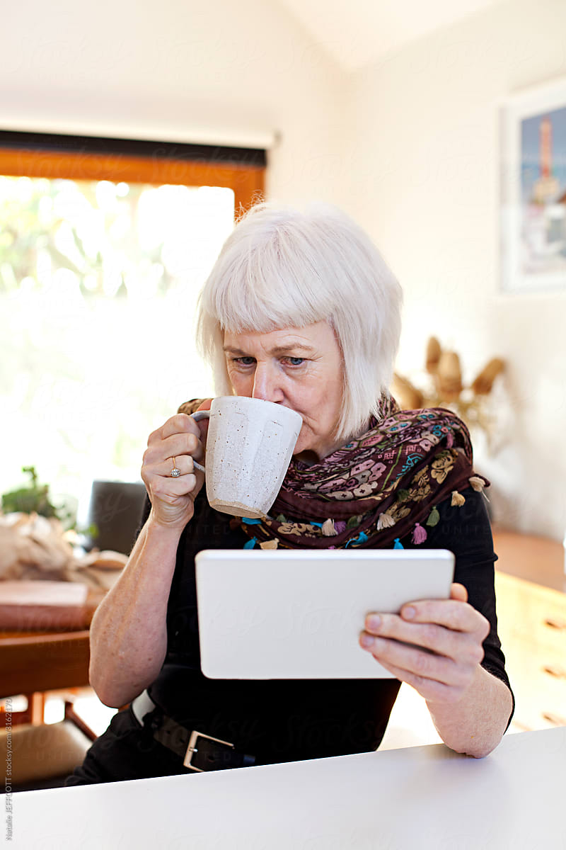 Senior woman in kitchen with coffee using touchpad