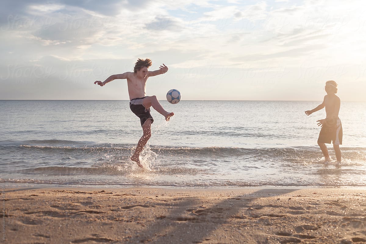 Teenage boys playing soccer on the beach by skye torossian for Stocksy Unit...