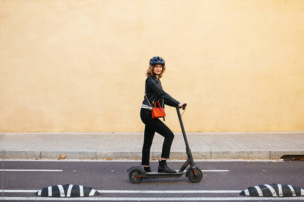 Stylish woman riding electric scooter on road