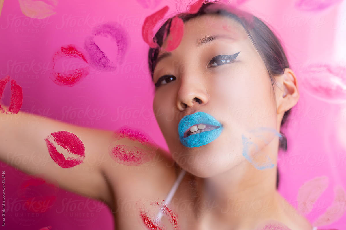 Woman with colorful makeup behind wall with kiss stains