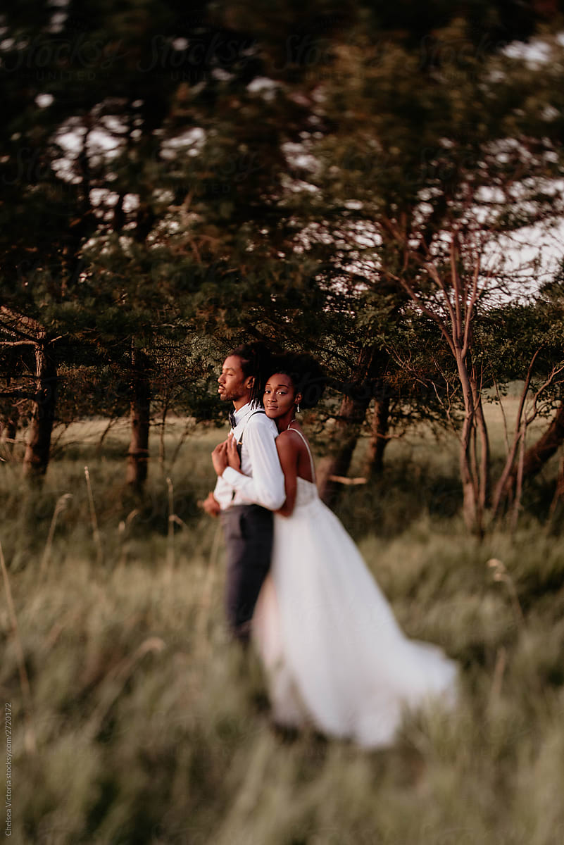 A beautiful young black bride and groom posing for portraits in a meadow on their wedding day