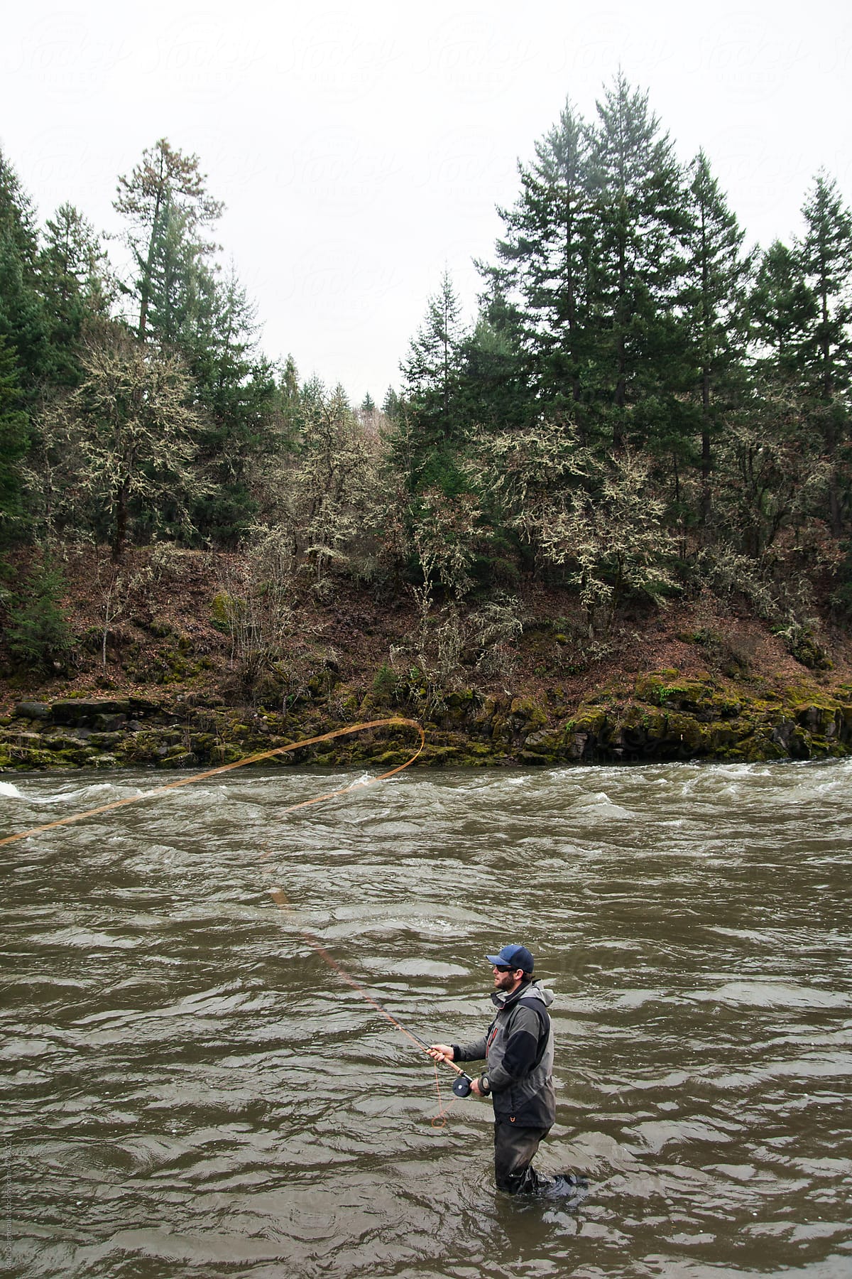 Man stands in the river casting an orange fly fishing line.