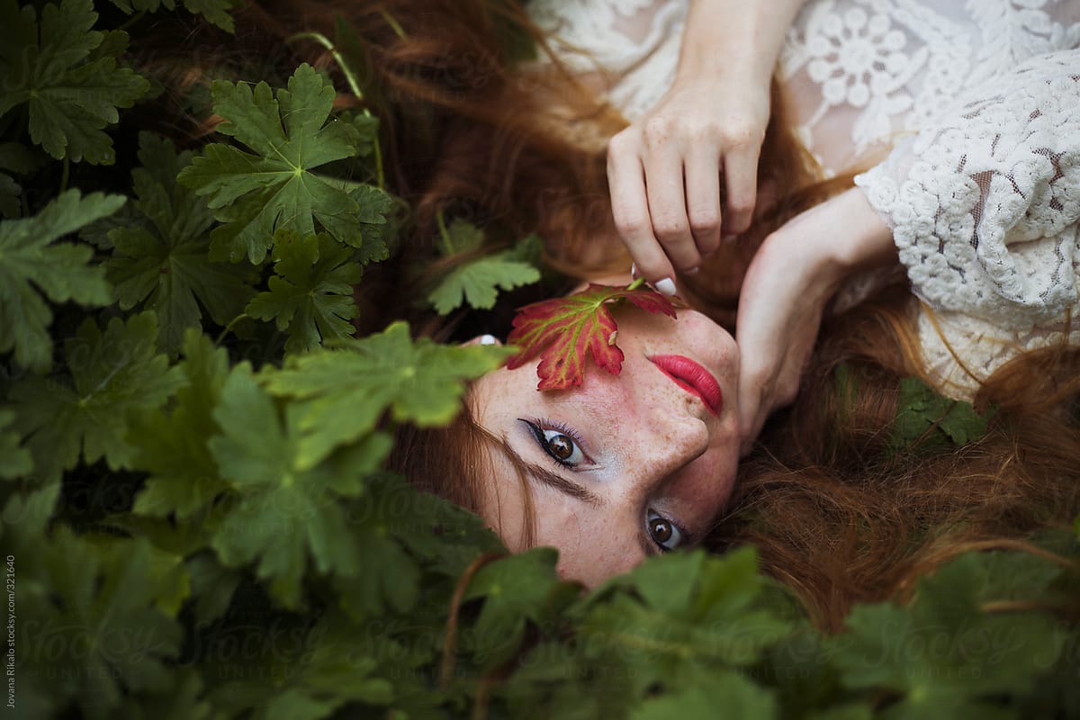 Portrait Of A Beautiful Young Woman Lying Down In Grass And Holding A Leaf By Stocksy