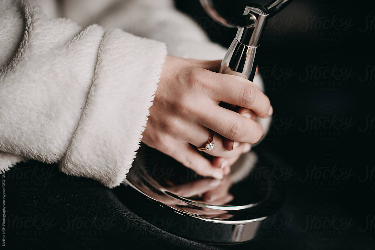 close up of bride in bathrobe holding a mirror with focus on engagement ring with diamond