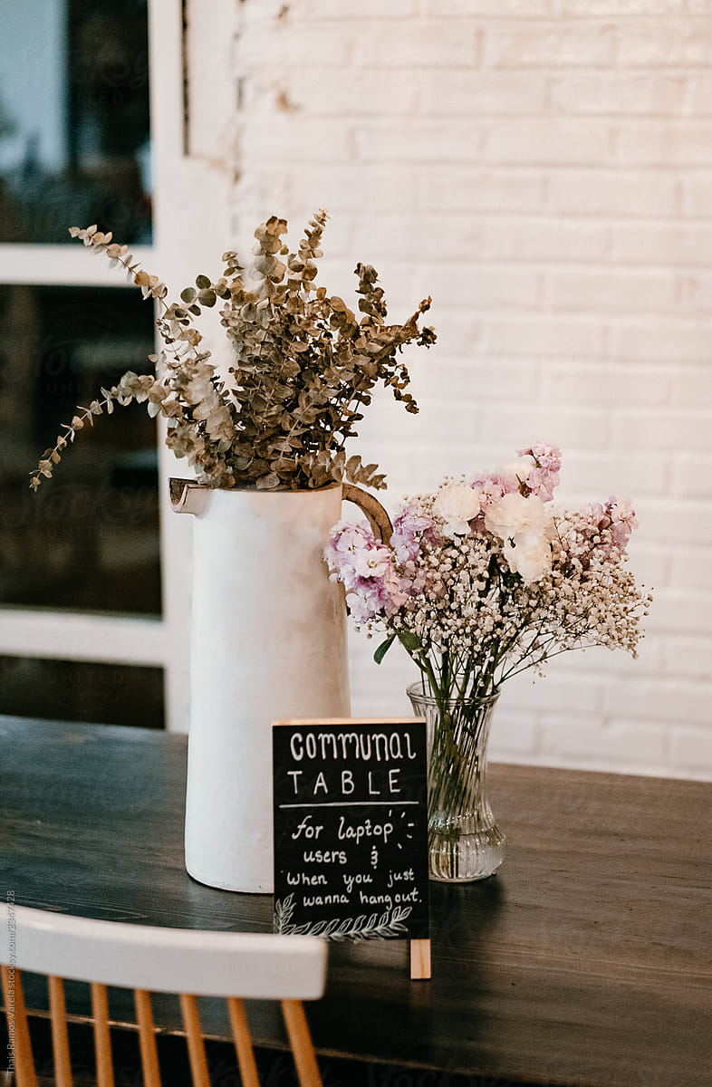 a table in a cafeteria decorated with a vase of flowers and with a message on a blackboard