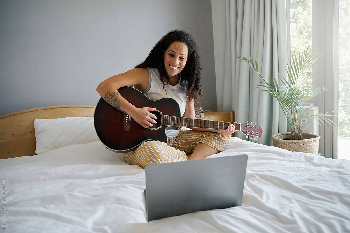 Happy young woman learning playing guitar on bed