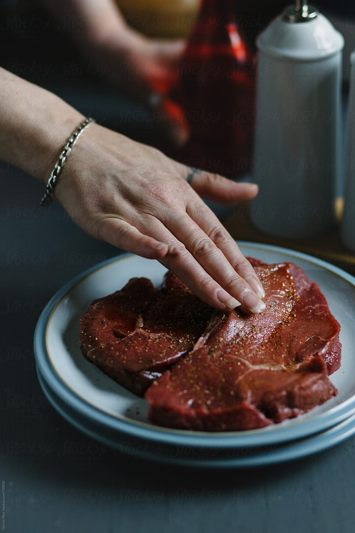 Woman\'s hand rubbing seasoning into beef steak on a plate.